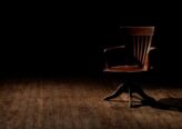 A vintage wooden chair is spotlighted in a dark studio setting, casting shadows.